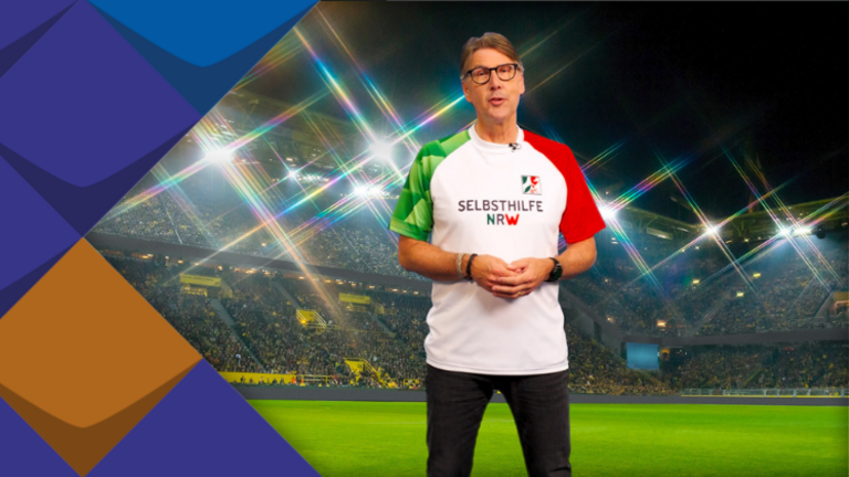 Sportmoderator Peter Großmann im Trikot mit der Aufschrift Selbsthilfe NRW