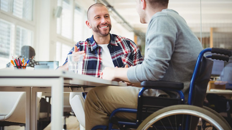 Man sieht zwei Männer, die miteinander sprechen. Der eine Mann sitzt im Rollstuhl